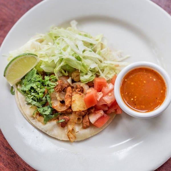 A Noche Mexicana taco with meat, onions, cilantro, lettuce, tomatoes, lime, and salsa.