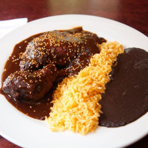 Noche Mexicana's chicken mole with sesame seeds, yellow rice, and refried beans on a white plate.