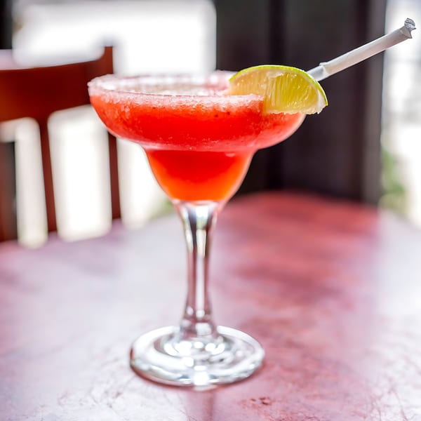 A vibrant red strawberry margarita with a salted rim, lime wedge, and straw on a table.