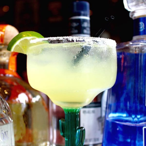 A Noche Mexicana margarita in a cactus glass, garnished with a lime and salt rim.