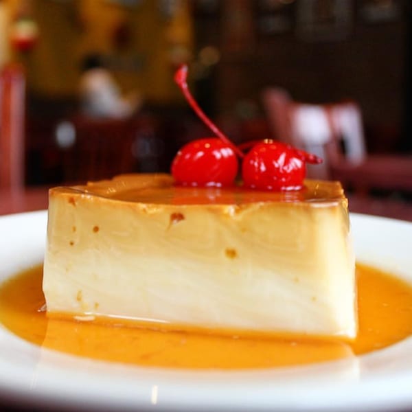 A slice of Noche Mexicana's flan dessert with caramel sauce and two maraschino cherries on top.