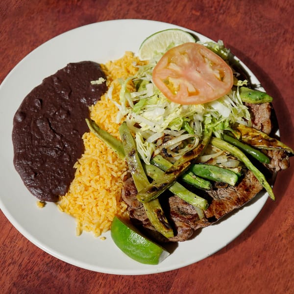 Noche Mexicana's carne asada with rice, refried beans, grilled peppers, and a lime wedge.