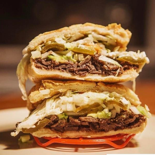 A stacked Mexican torta sandwich with shredded meat, lettuce, onions, and pickled jalapeños.