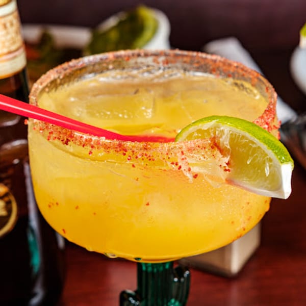 A Noche Mexicana margarita with a chili-lime rim, lime wedge, and red straw.